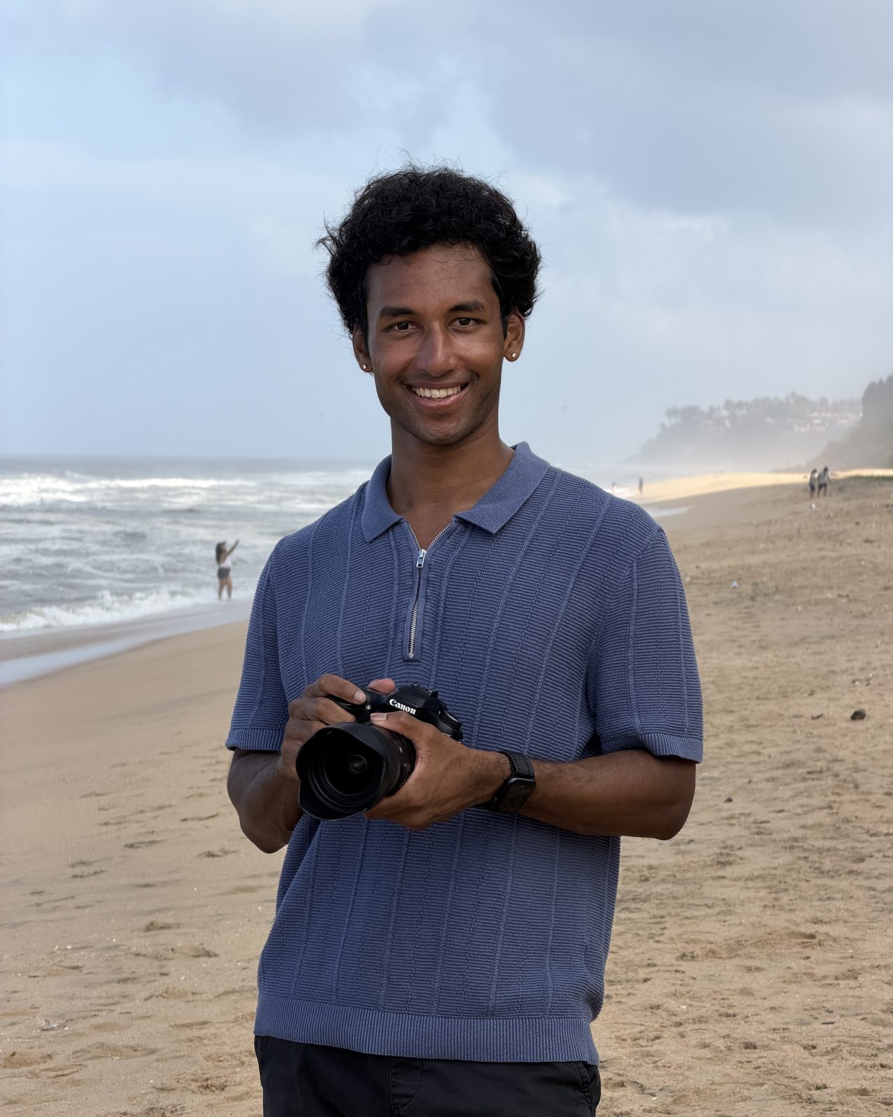 Sai Kasam on the beach, smiling, holding a camera